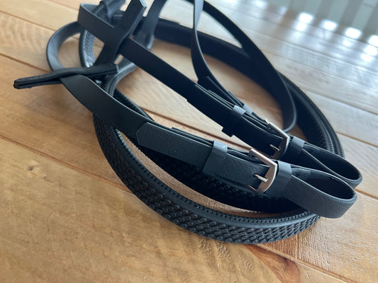 A close-up of LS Equestrian's Reins Pimple Grip, showcasing coiled black leather with stainless steel fittings and visible textures on a wooden surface.