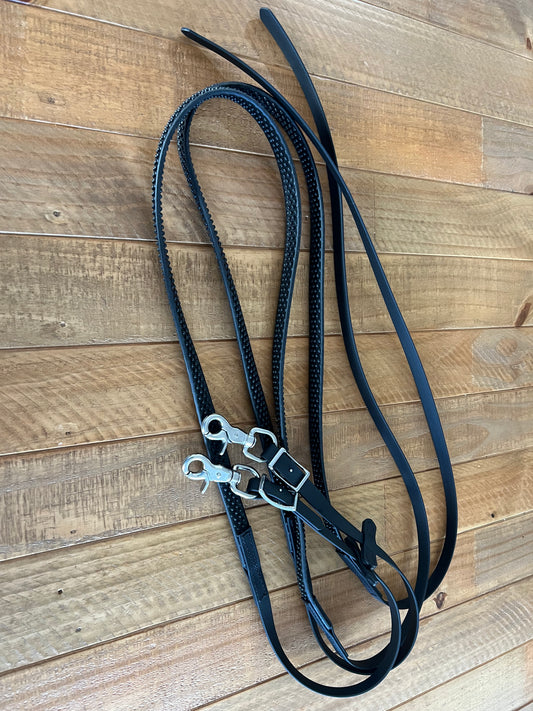 Displayed on a wooden surface is a set of Split Reins Soft Grip - Design your own by LS Equestrian, featuring stainless steel fittings and rectangular buckles in black leather.