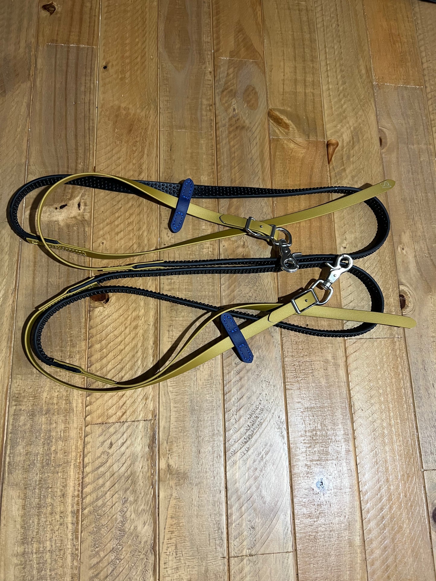 A pair of customized "Split Reins Soft Grip - Design your own" by LS Equestrian, featuring a yellow and black BioThane with stainless steel fittings, rests neatly folded on a wooden floor.