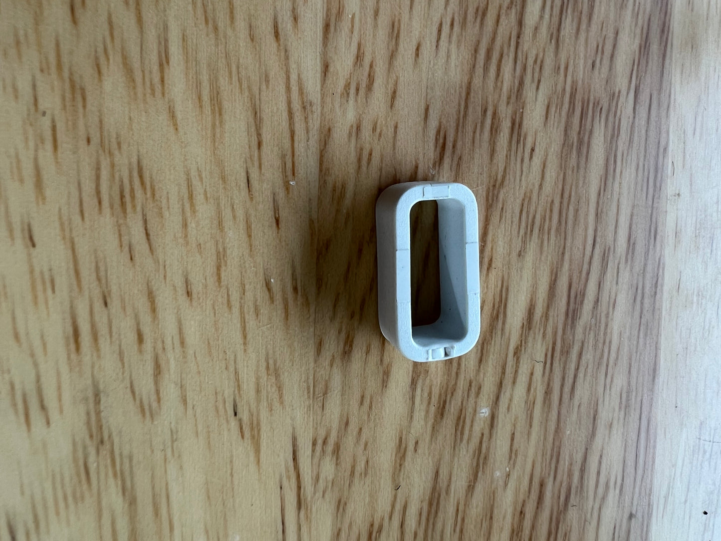 A limited stock White loop keeper - 16mm from LS Equestrian, characterized by its small, white, oval-shaped plastic design with a hollow center, is placed on a wooden surface.