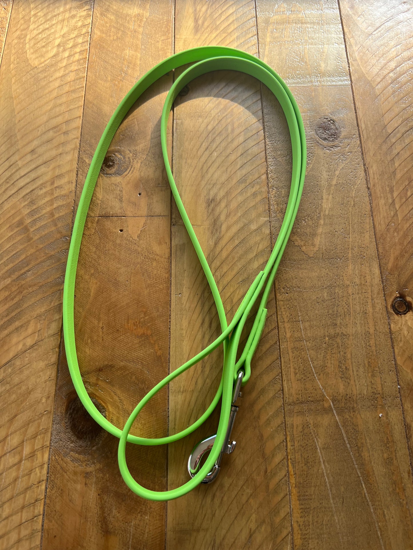 An Apple Green dog lead from LS Equestrian, featuring super heavy nickel fittings, is neatly coiled on a wooden surface with a natural grain pattern.