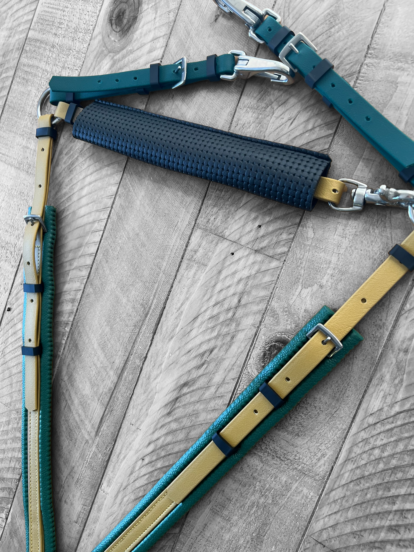 Close-up of the LS Equestrian Breastplate Wither / Neck Strap Protector, featuring multicolored straps in teal, navy, and mustard on a wooden surface. Equipped with metal buckles and waffle padding for style and comfort, its modern design includes a textured section perfect for those seeking a fashionable breastplate protector.