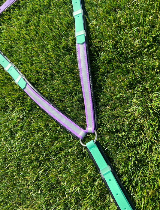 Colorful BioThane® straps in purple and mint green from LS Equestrian's Customisable Reflective Breastplates are arranged on lush grass, intersecting at a central metal ring—ideal for crafting safe and durable horse tack.