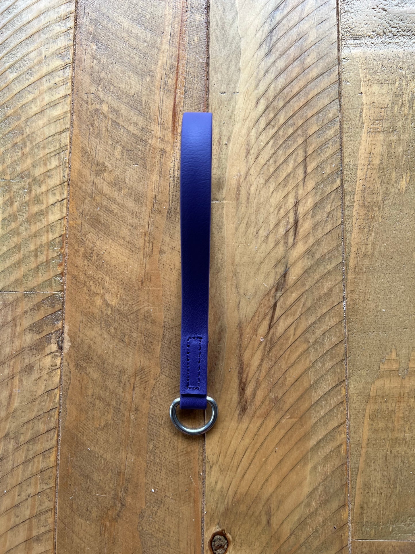 The Girth Loop - Design your Own keychain by LS Equestrian, featuring a purple leather finish and a sturdy metal ring, rests on a textured wooden surface reminiscent of an elegant breastplate design.