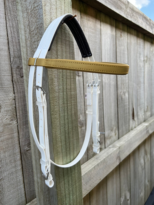 A custom-designed Hackamore BioThane®️ Bridle from LS Equestrian, featuring a white and tan color scheme with metal buckles, is draped over a wooden fence. The BioThane®️ material enhances the rustic charm of the weathered wood, with the partly visible sky providing a tranquil background.
