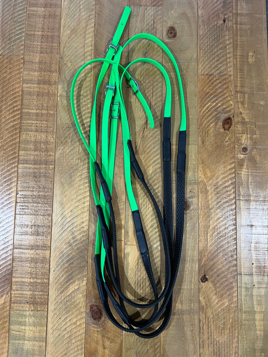 A set of LS Equestrian's Soft Grip Non Split Reins - Design your Own, customized in green and black, is laid out on a wooden floor. These reins are expertly crafted from a blend of leather and elastic materials, featuring BioThane construction with durable stainless steel fittings for added elegance and strength.