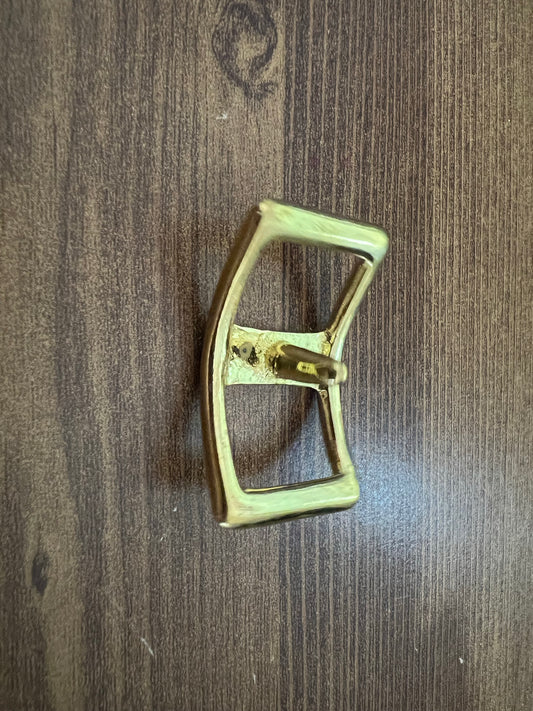 A Conway Buckle by LS Equestrian, crafted from brass in a rectangular shape with rounded edges, lies elegantly on the wooden table surface.