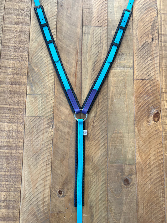 A teal and purple leather padded breastplate by LS Equestrian, custom made with adjustable straps, is displayed on a wooden surface. The symmetrical Y shape features metal clasps and buckles for easy adjustment, ensuring a perfect fit.