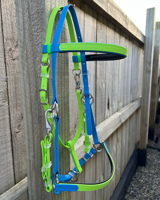 An eye-catching LS Enduro Bridle - Apple & Cyan from LS Equestrian is draped over a wooden fence. The neon green and blue straps are complemented by the metal buckles and clips, which stand out against the colorful custom design, proudly crafted in New Zealand.