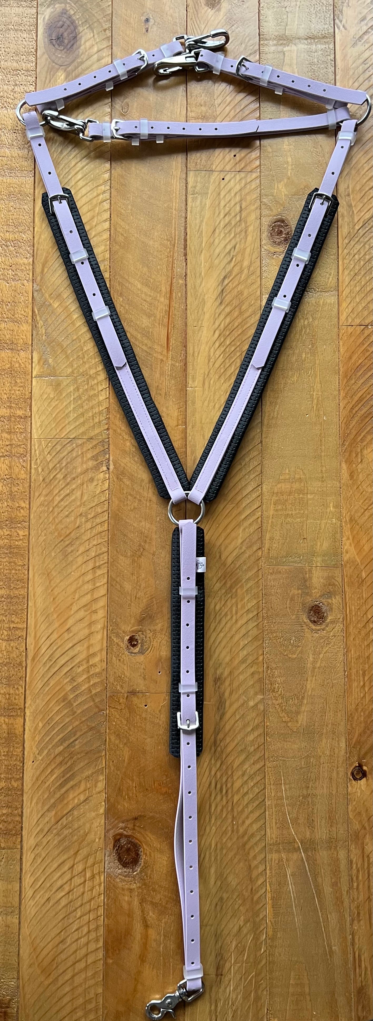 The LS Equestrian Padded Breastplate - Lavender, crafted from durable BETA BioThane material in purple and black with metal rings and buckles, is displayed on a wooden surface.