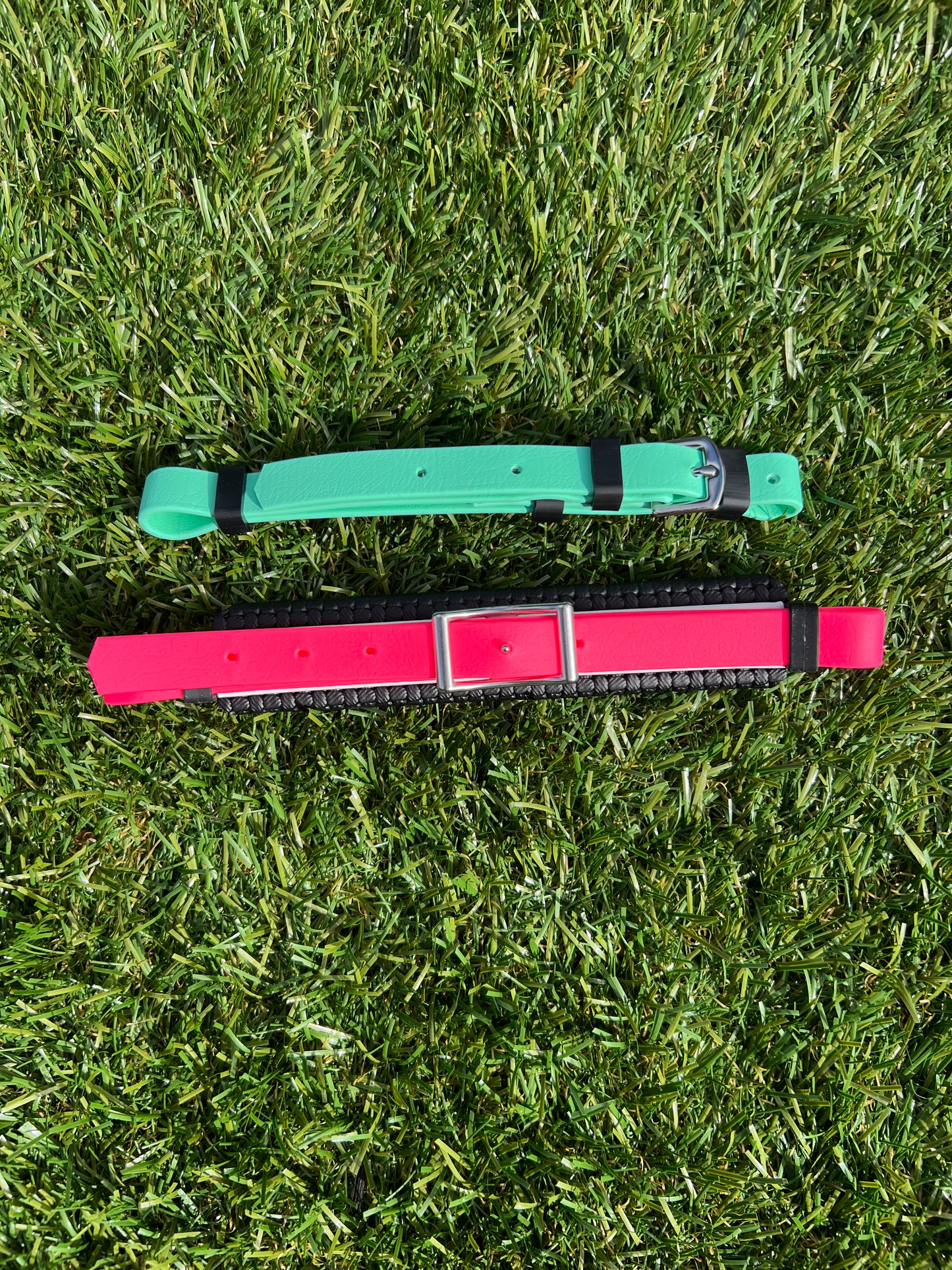 Two pet collars lie on the grass. The top collar, with a BETA finish, is green with a black buckle, while the bottom one is red featuring stainless steel fittings and a metallic buckle from LS Equestrian's Hackamore Padding Replacement Set collection.
