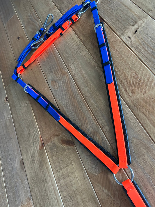 The Customisable BioThane® Breastplate by LS Equestrian is vibrant and durable, featuring blue and orange straps with black accents, metal rings, and buckles, coiled in matching colors for style and strength