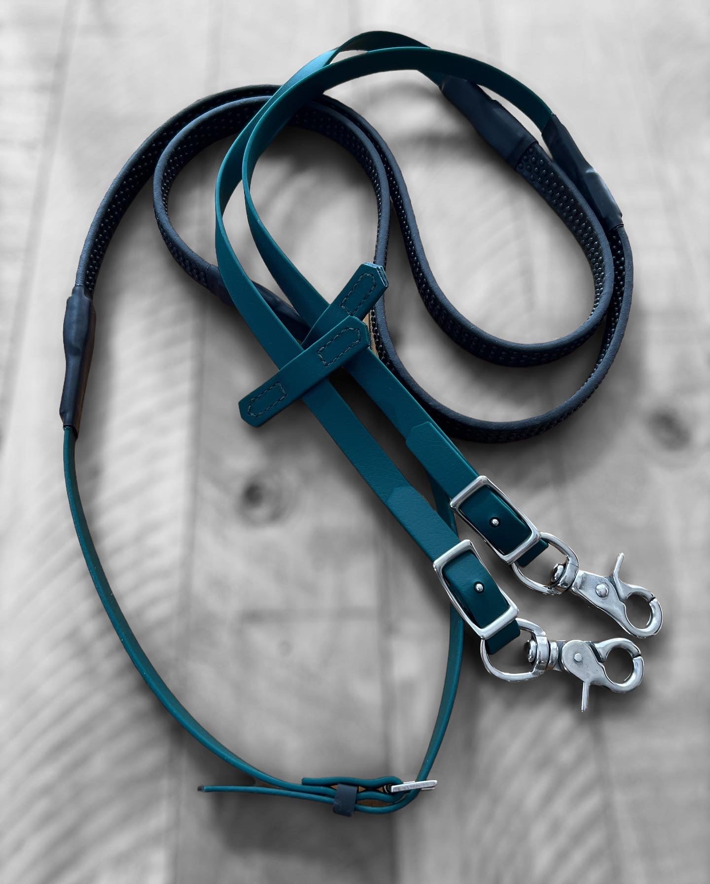 A hunter green leather rein from the LS Equestrian collection, featuring silver clasps and brown accents, lies coiled on a wooden surface.