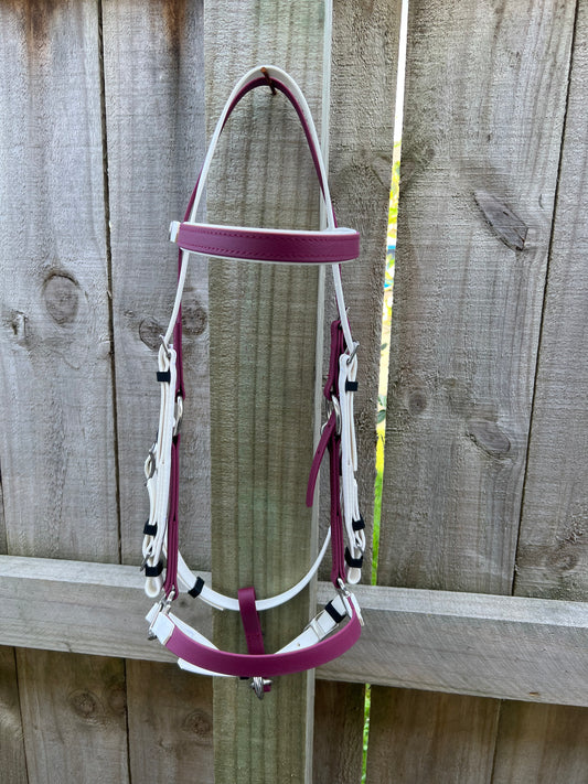 A maroon and white LS Deux Bridle by LS Equestrian is hanging on a wooden fence. The bridle, ideal for endurance riding, features silver buckles and is neatly draped over the top, showcased against the rustic wood background.