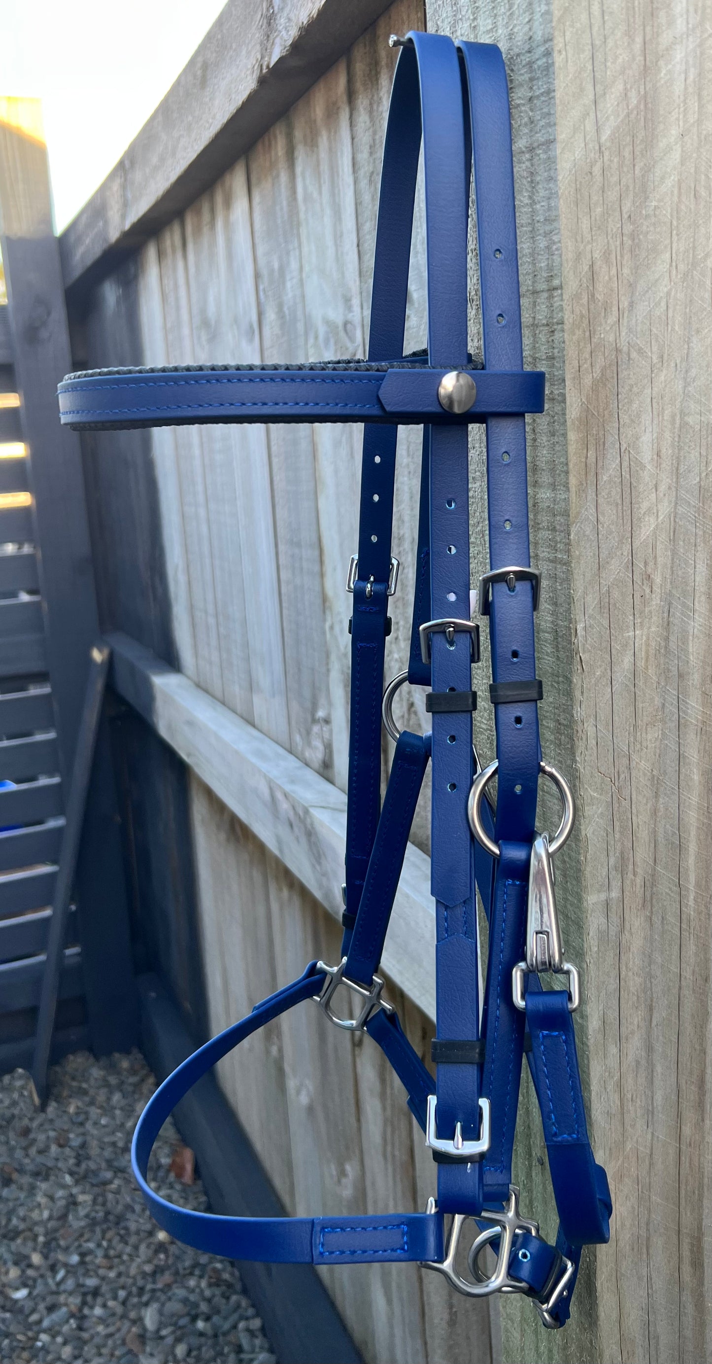 A navy LS Equestrian 2 Part Bridle with silver hardware hangs gracefully on a wooden fence.