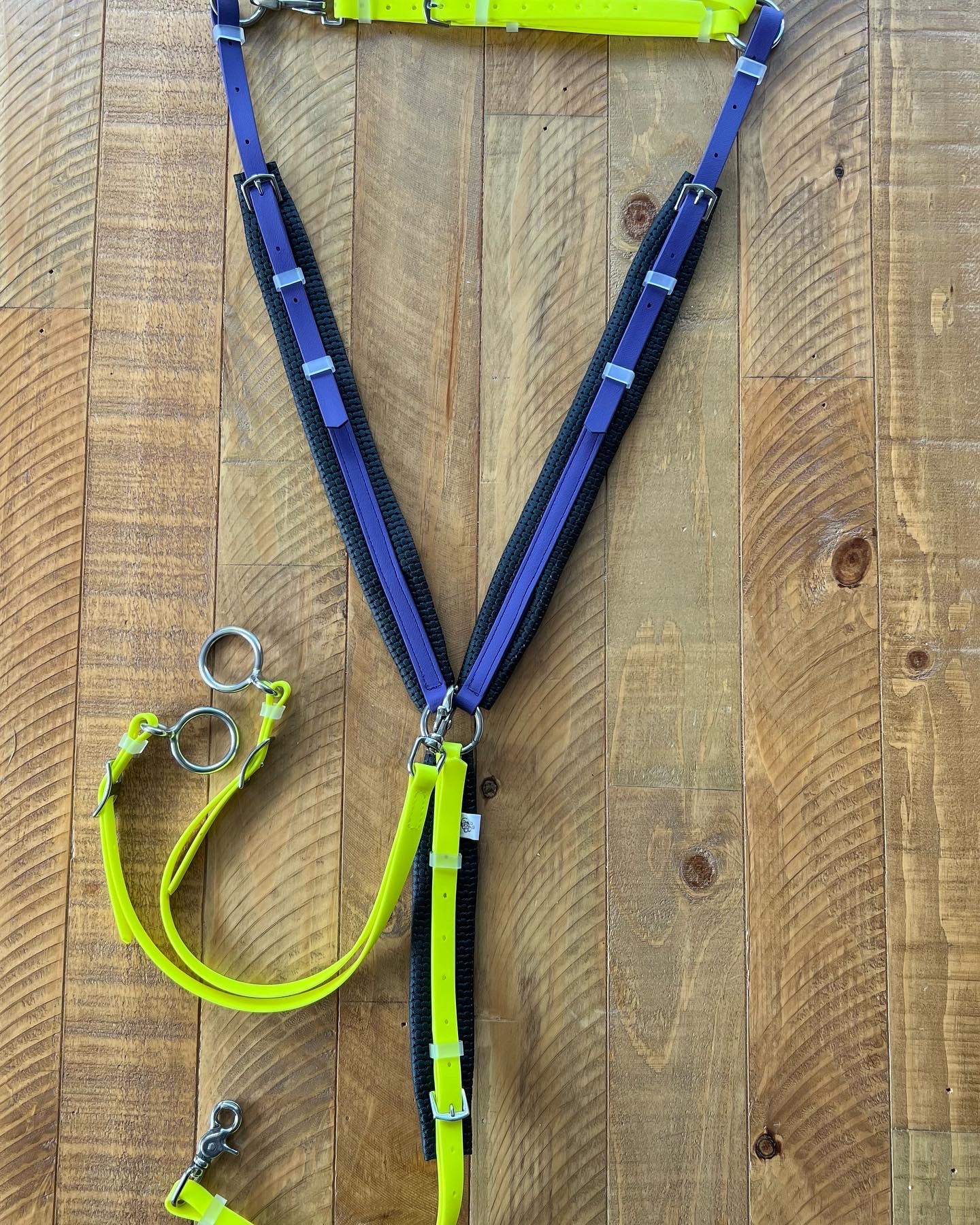 An eye-catching horse harness with a BETA finish from LS Equestrian is laid out on a wooden floor, showcasing vibrant Fluro Yellow and black straps. It includes metal rings, adjustable buckles, and features a versatile Martingale attachment to enhance its functionality. Note that the breastplate is not included in the price.