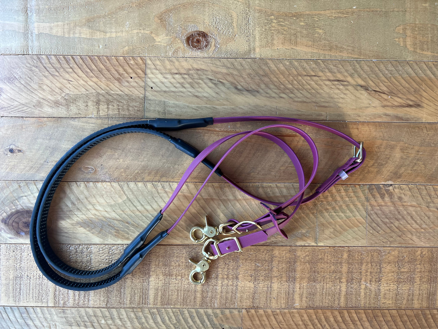 A set of Soft Grip Reins by LS Equestrian, featuring maroon sections, sits on a wooden surface, custom crafted with gold metal clasps and buckles.