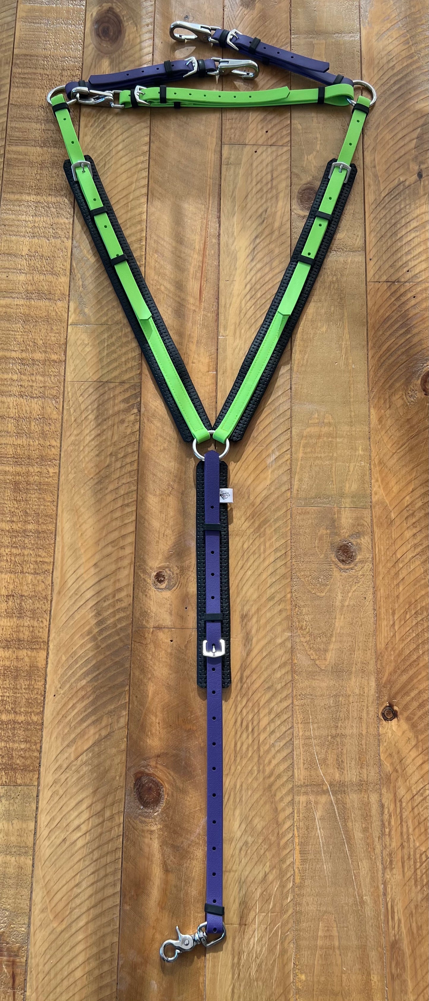 The LS Equestrian Padded Breastplate in Apple Green and Purple showcases vibrant BioThane straps elegantly arranged on a wooden surface. Expertly crafted with multiple buckles and metal clips, it's designed for both style and durability.