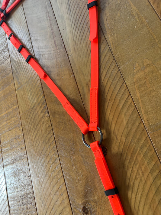 A Breastplate Zero Padding in bright orange from the LS Equestrian range is laid out on a wooden floor, showcasing its adjustable straps and sturdy metal ring connecting two sections.