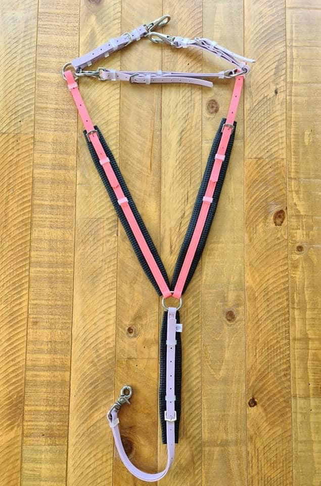 The LS Equestrian Breastplate in Coral & Lavender, crafted from durable BETA® BioThane®, with assorted straps and buckles, is laid out flat on a wooden surface.