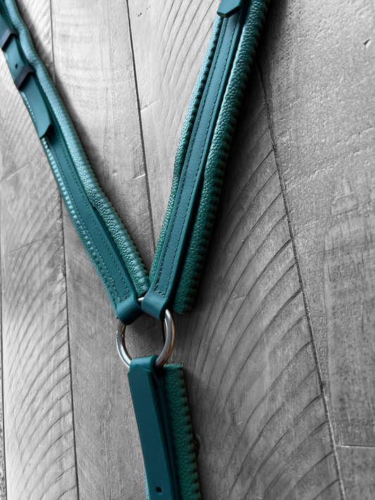 Close-up of the Padded Breastplate - Green on Green with silver rings hanging on a wooden wall. The texture of the wood contrasts with the smooth, durable material from LS Equestrian.