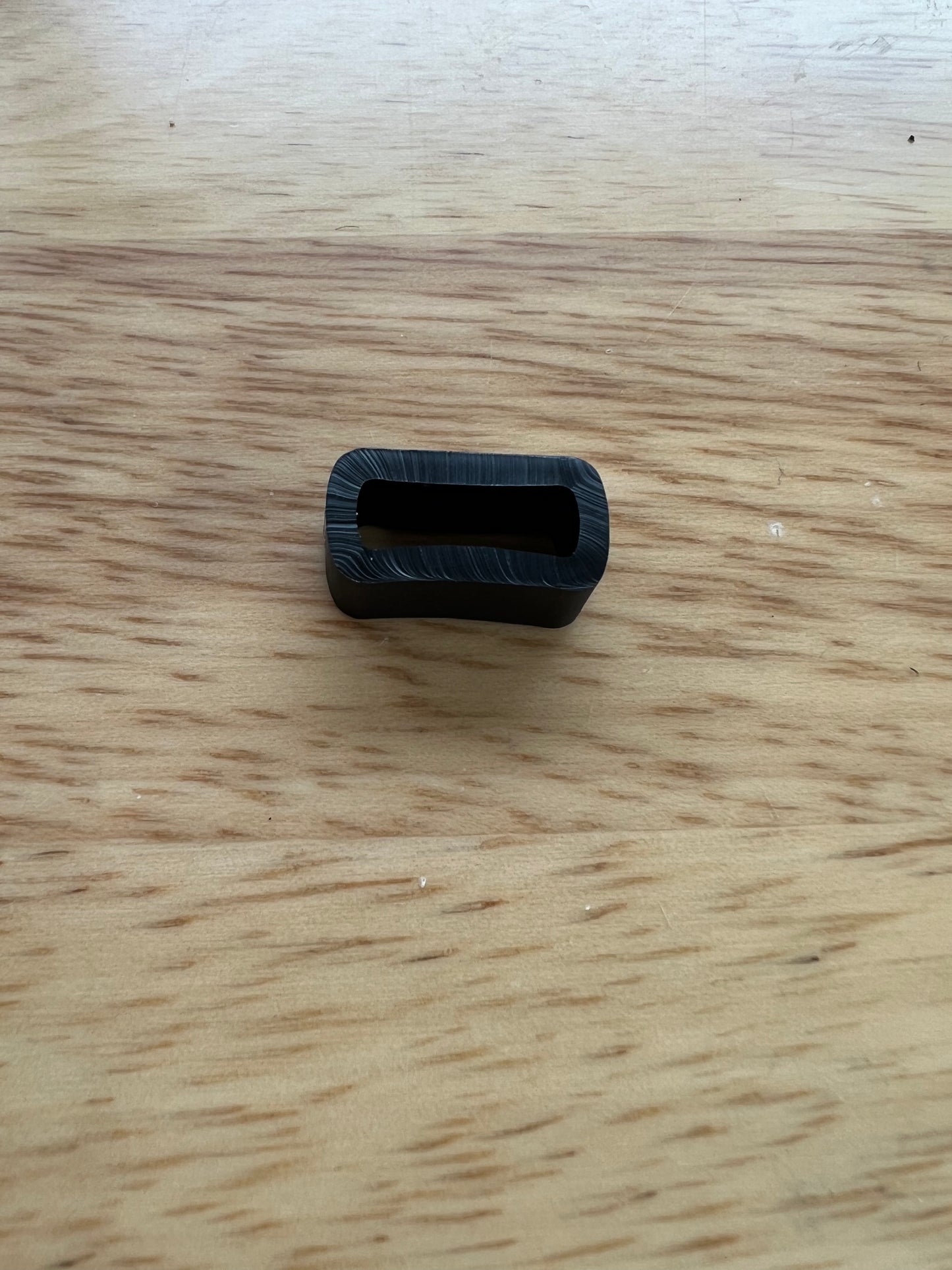 A small, oval-shaped object with a rectangular cutout from LS Equestrian, the 16mm Black Loop Keeper, lies on a wooden surface.