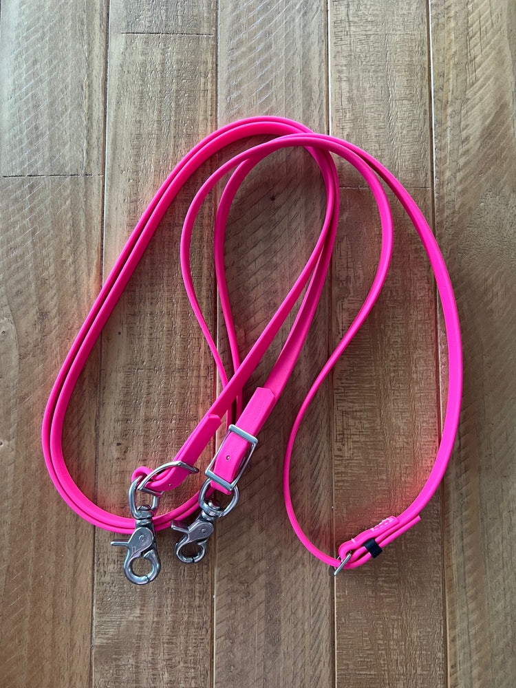 A bright pink dog leash with metal clasps lies coiled on a wooden floor.