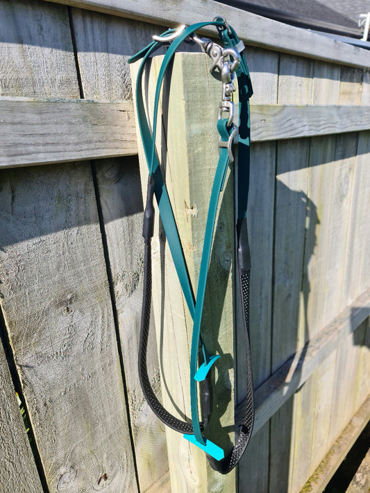A hunter green and black rein from the LS Equestrian collection, featuring silver hardware, hangs on a wooden fence in bright sunlight, casting a shadow on the boards. The custom-made rein appears slightly tangled.