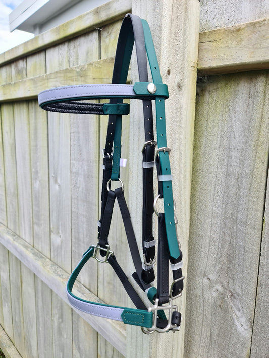 A hunter green, black, and grey horse halter from the LS Equestrian LS Deux range, complete with silver buckles, hangs on a wooden fence. It features a white trim along the noseband and headpiece, crafted from durable materials ideal for endurance riding.