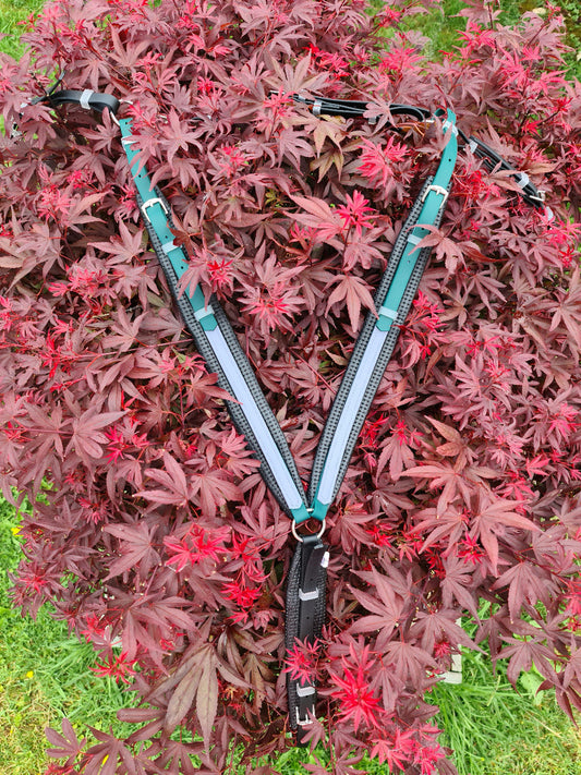 A Padded Breastplate in hunter green, black, and grey from LS Equestrian is elegantly draped over a bush with vibrant red leaves, showcasing its custom-made design with SS or brass fittings.
