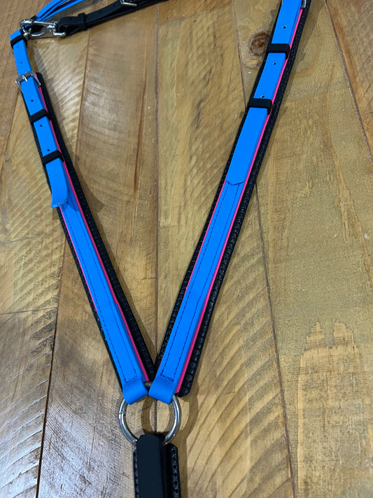 Close-up of a vibrant, custom-made harness on a wooden surface. Featuring LS Equestrian materials, the 2 Toned Padded Breastplate boasts cyan, hot pink, and black straps with sturdy metal rings and buckles—a testament to New Zealand craftsmanship.