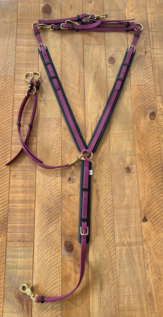 A set of LS Equestrian Martingale in maroon with brass hardware, featuring a BETA finish. The design includes adjustable straps and clips forming a V-shape pattern, complete with a martingale attachment, all elegantly arranged on a wooden surface. Note: Breastplate not included in price.