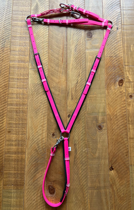 A Padded Breastplate in Hot Pink by LS Equestrian is laid out on a wooden surface. Part of the LS Enduro range, this custom-made piece features adjustable straps and metallic buckles for the perfect fit.