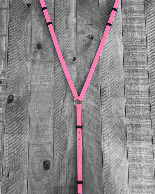A Coral Pink Breastplate Zero Padding from LS Equestrian, crafted with durable BioThane® and featuring a Y-shape with black accents, is laid out on a rustic wooden background.