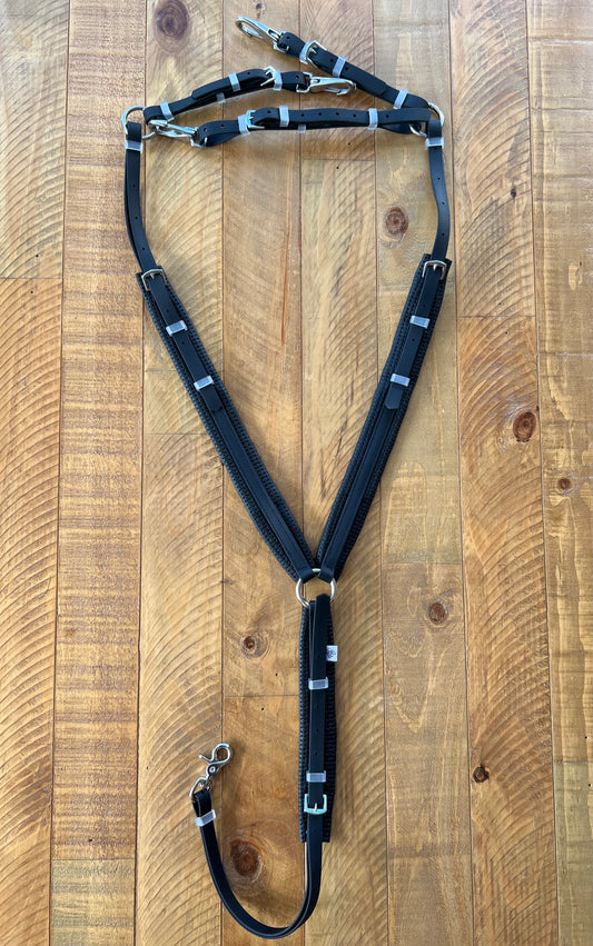 A black LS Equestrian horse harness made from BETA® BioThane® with metal buckles and clips is arranged on a wooden surface, accompanied by its matching breastplate, highlighting its structure and design.