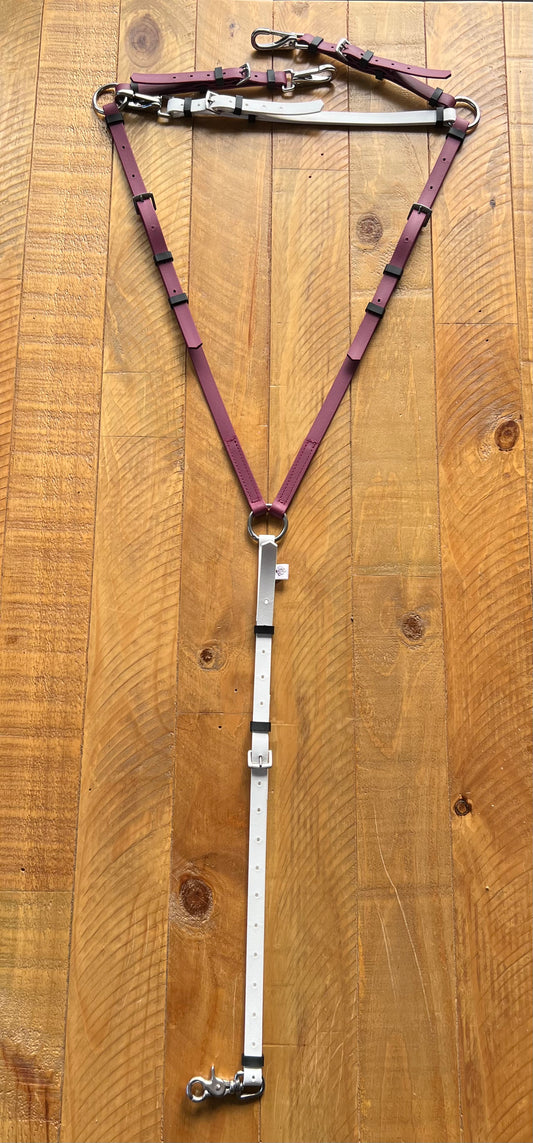 A maroon and white BioThane Breastplate Zero Padding from LS Equestrian is shaped like a 'Y' on a wooden surface, with its sections connected by metal rings and buckles.