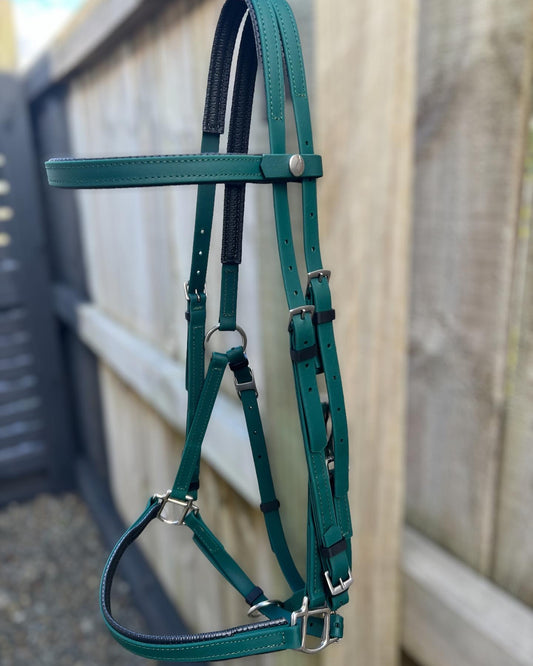 A hunter green LS Equestrian Padded LS Deux Bridle hangs on a wooden fence, showcasing silver buckles and adjustable straps with padding for comfort—ideal for endurance riding.