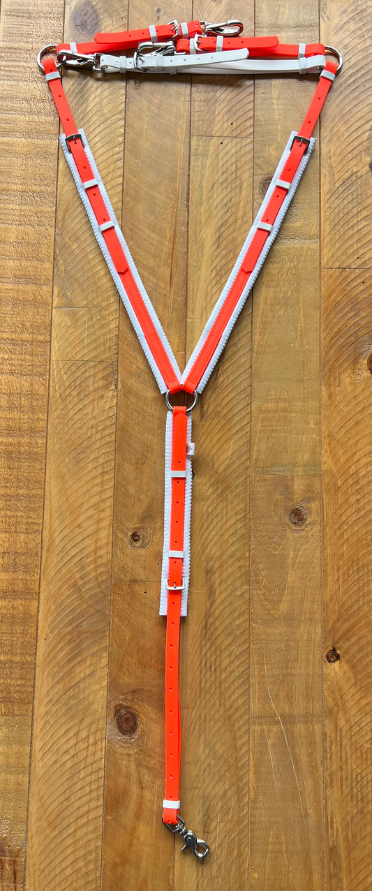 A Padded Breastplate - Fluro Orange & White from the LS Equestrian collection is arranged on a wooden surface. This custom-made design, featuring reflective strips, includes metal rings for attachments and adjustable buckles, forming a Y-shape ideal for any adventure.