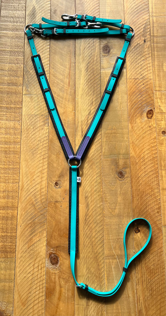 The LS Equestrian Padded Breastplate in teal and purple, constructed with BioThane for enhanced durability, includes adjustable straps and silver buckles. It is stylishly displayed on a wooden surface.