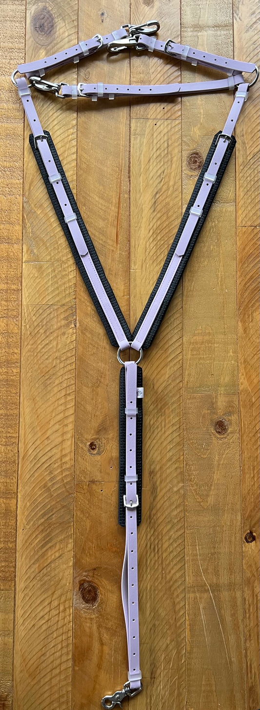 The LS Equestrian Padded Breastplate - Lavender, crafted from durable BETA BioThane material in purple and black with metal rings and buckles, is displayed on a wooden surface.