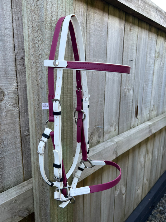 The LS Deux Bridle from LS Equestrian, in maroon and white, hangs elegantly on a wooden fence. Its shiny metal buckles accentuate the simple design, making it an ideal choice for endurance riding. The bridle's colors contrast beautifully against the slightly weathered wooden planks.