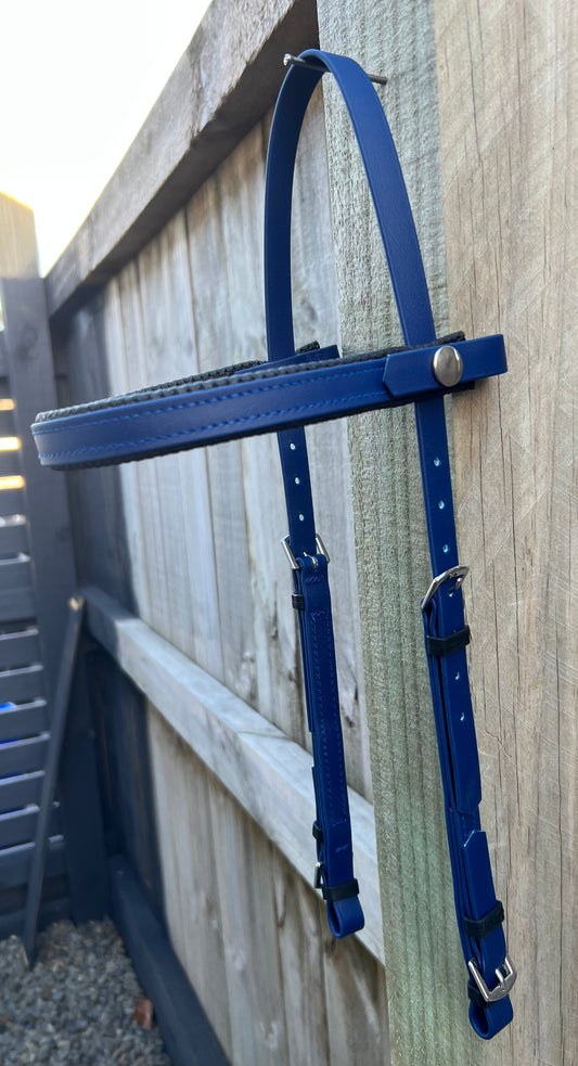 A navy leather bicycle carrier leans gracefully against a wooden fence, its adjustable straps reminiscent of the elegant 2 Part Bridle by LS Equestrian, featuring polished metal buckles. The sun shines softly, evoking a serene outdoor setting.