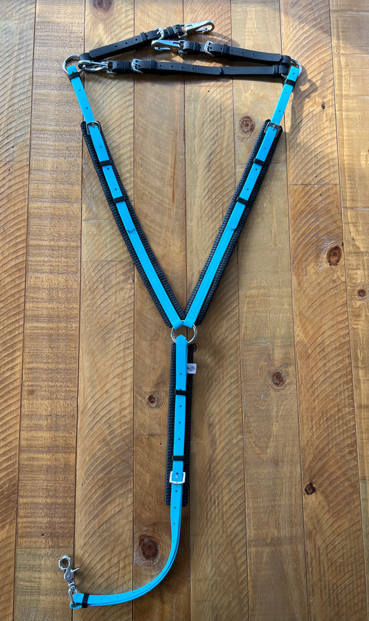 A light blue and black LS Equestrian Padded Breastplate is displayed on a wooden surface. This Y-shaped piece from the LS Enduro range features brass fittings, along with metal buckles and clips for secure attachment, combining durability with style.