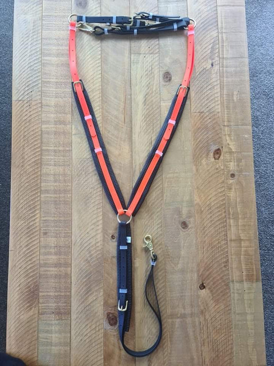 A Padded Breastplate in Fluro Orange and Black is neatly displayed on a wooden table. This LS Equestrian product from New Zealand features metal buckles and comes with a detachable leash clip, arranged symmetrically.