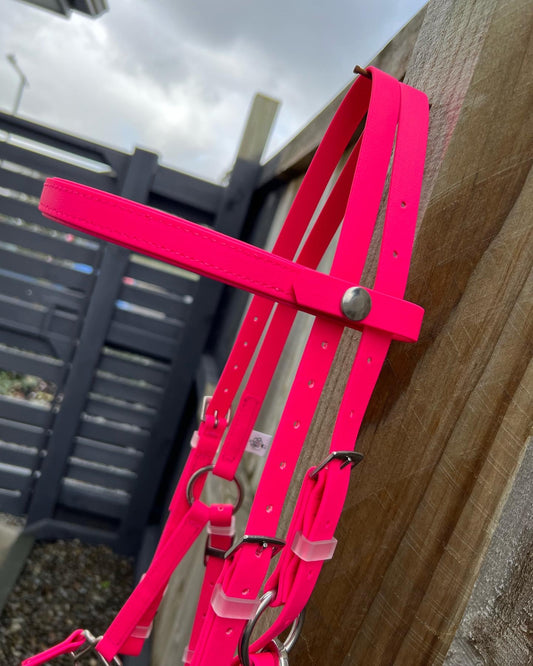 The LS Deux Bridle in Hot Pink from LS Equestrian is a versatile piece crafted from Beta BioThane, displayed on a wooden fence. A gray slatted fence and cloudy sky serve as the backdrop. Featuring silver hardware and adjustable straps, this bridle is perfect for everyday use.